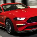 Red Ford Mustang GT speeding through a tunnel, headlights and grill lit in motion.