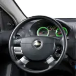 Inside view of a Chevrolet car dashboard, steering wheel centered with logo and illuminated green gauges behind it.