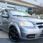 Front-left three-quarter view of a gray Chevrolet compact car with black rims parked outside a dealership.