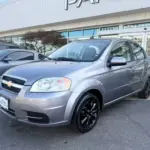 Silver Chevrolet sedan parked in a dealership lot, front three-quarter view near the showroom, black alloy wheels visible.
