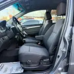Interior of a gray car showing the driver and front passenger seats, steering wheel, and dashboard from the open driver's door.
