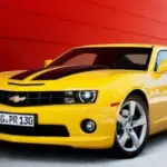 Yellow Chevrolet Camaro with black racing stripes parked in front of a red wall. (informative)