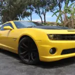 Yellow Chevrolet Camaro sport muscle car with a black hood and large black wheels parked on a driveway.