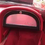 Close-up of a pink and chrome dashboard in a red vintage car, with red carpet and part of the steering wheel visible.